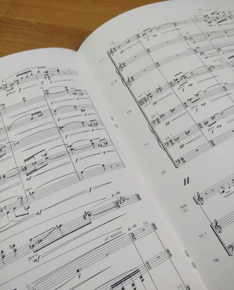 Open music score on wooden surface showing musical notation across multiple staves and pages