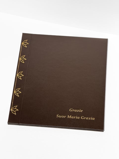Brown hardcover book with gold leaf decorations on spine and text reading Grazie Suor Maria Grazia