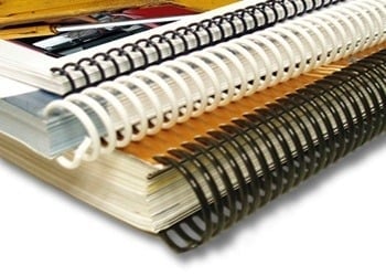Stack of spiral-bound notebooks in various colors including yellow, white, black, and brown with metal and plastic bindings