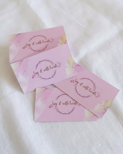 Four pink business cards with watercolor details and decorative circular design displaying say it with beads text