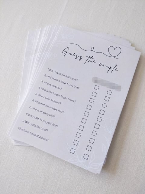 Stack of printed Guess the Couple trivia game cards with questions and checkbox answer grids on white background