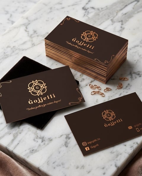 Goljerii luxury business cards with gold foil logo on dark brown cardstock displayed on marble surface