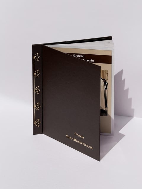 Open book with dark brown cover featuring decorative leaf patterns and Italian text Grazie displayed on white background