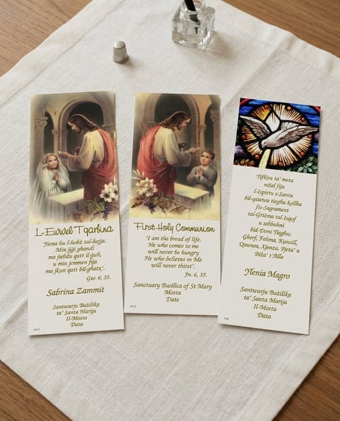 Three religious prayer cards displayed on a white linen cloth, featuring communion, Mary, and a dove with text in multiple languages