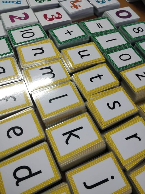 Close-up of alphabet tiles with yellow borders and number tiles with green borders arranged on a surface