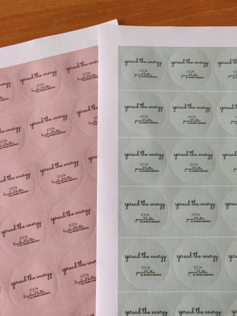 Sheets of stickers with spread the energy text on pink and green backgrounds arranged on a wooden surface