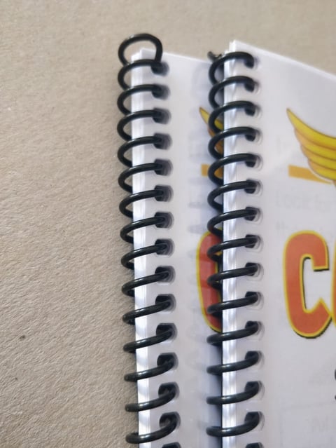 Close-up of a spiral-bound notebook with black metal coils and white pages, resting on a beige surface