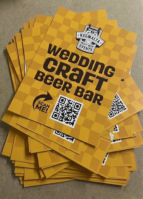Stack of yellow wedding craft beer bar promotional flyers with QR codes and Kegman brewery logo on concrete surface