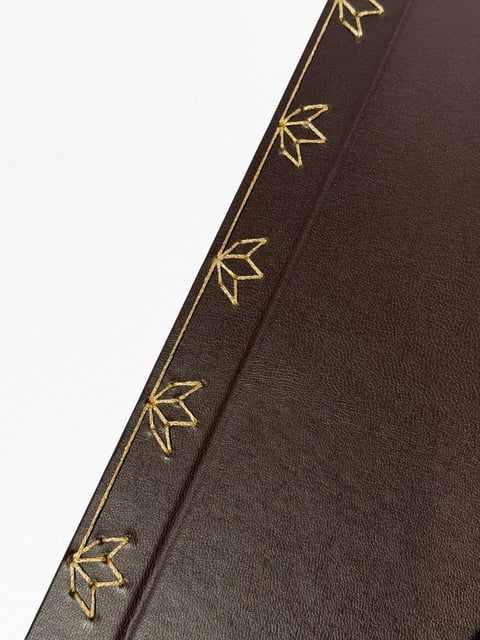 Close-up of dark brown fabric with gold leaf embroidery trim running along the edge