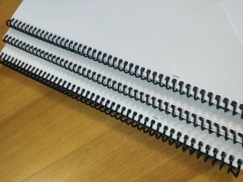 Five black spiral binding coils arranged in a row on a wooden surface with white paper