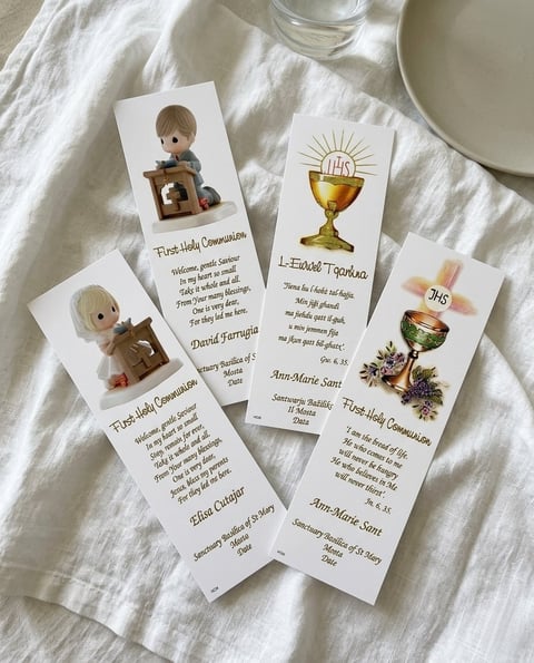 Four commemorative prayer cards with religious illustrations arranged on a white linen cloth, featuring First Holy Communion and Eucharist themes